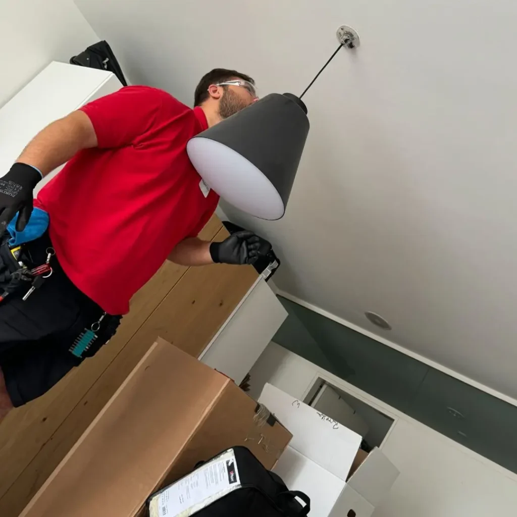 Techniker montiert eine Lampe sowie Lichtschalter und Steckdose.